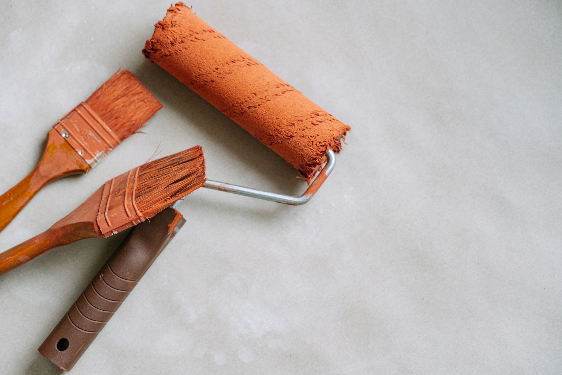 Two paint brushes and an orange paint roller on a light surface, ideal for DIY and home improvement concepts in Pasadena, CA
